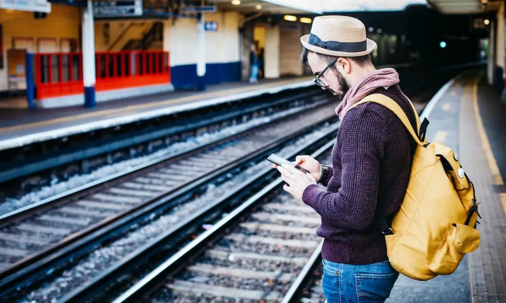 man using phone while standing in front of train rail during daytime