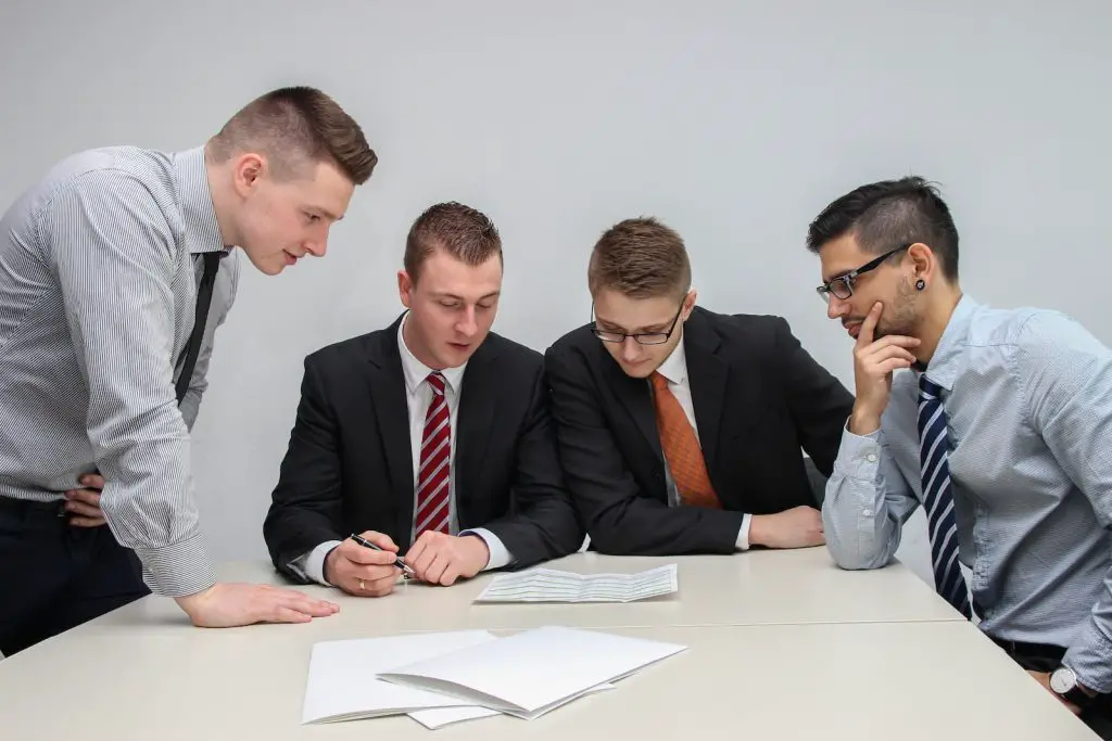 four men looking to the paper on table-Team Leader
